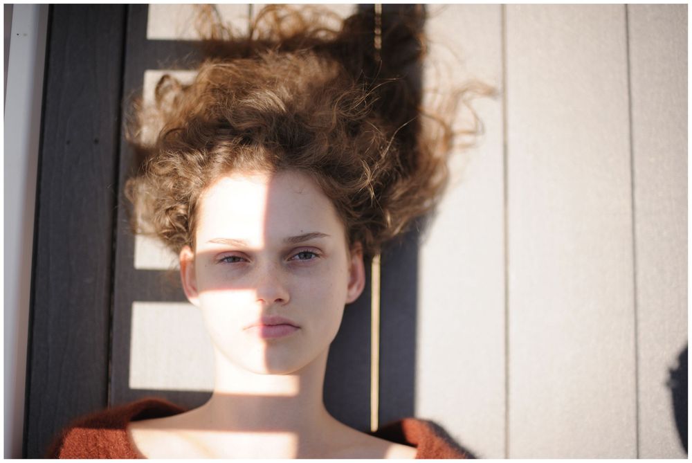 Woman with voluminous curly hair lying down near window with natural lighting in artistic portrait.
