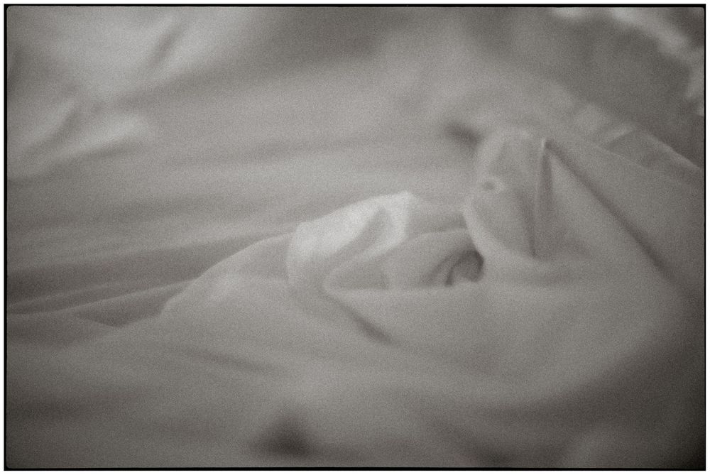 Close-up black and white photo of crumpled white bed sheets with soft shadows.