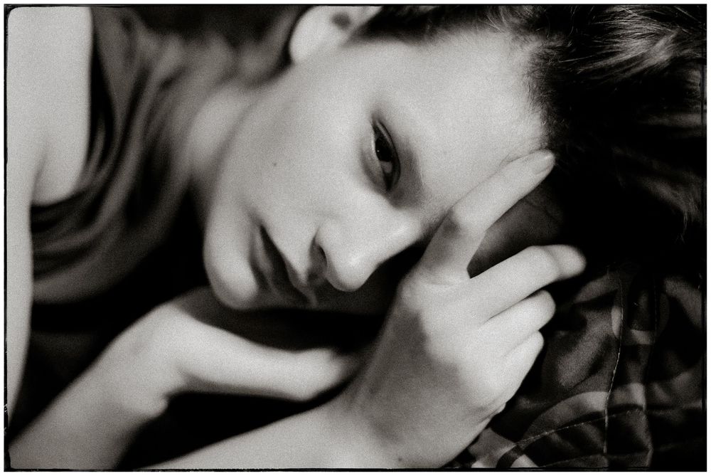 Black and white portrait of a young woman with dark hair resting her head on her hand in a contemplative pose.