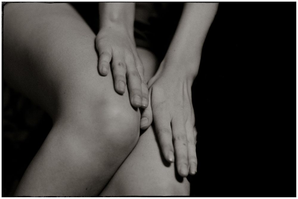 Black and white close-up photograph of hands resting on bare knees in a contemplative pose.