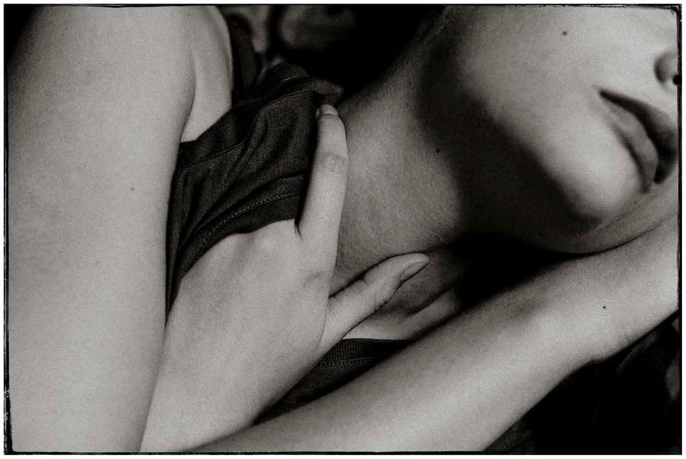Black and white intimate photo of a woman resting with a hand gently placed on her chest.