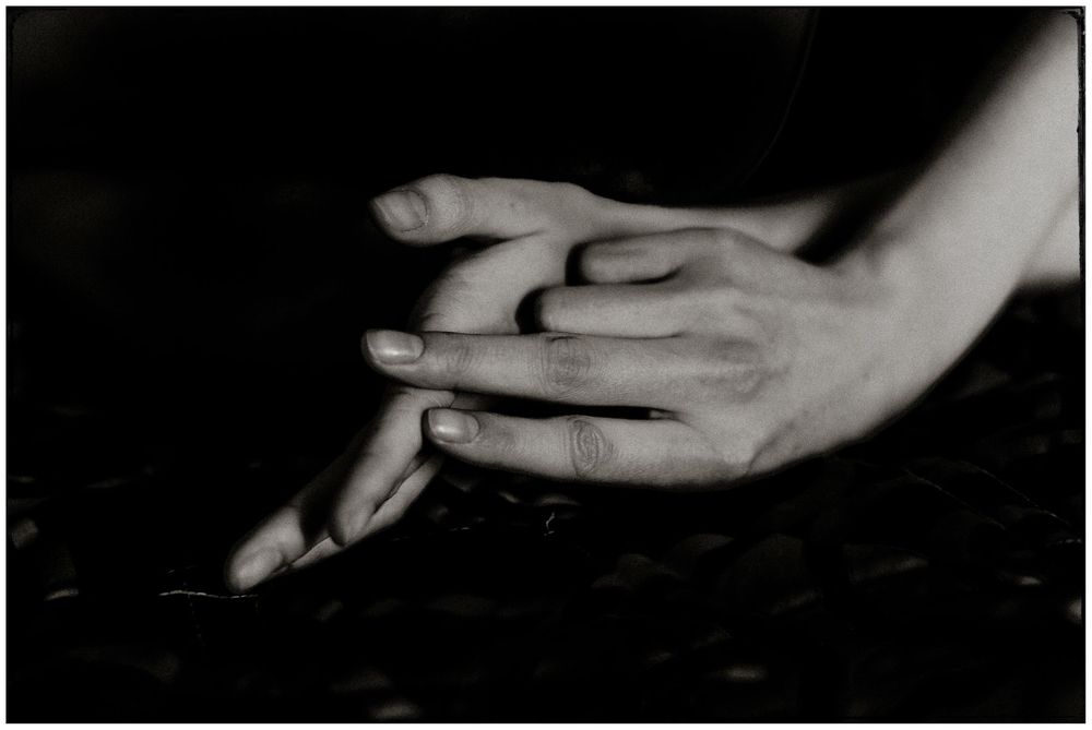 Close-up black and white photo of two hands gently intertwined against a dark background.