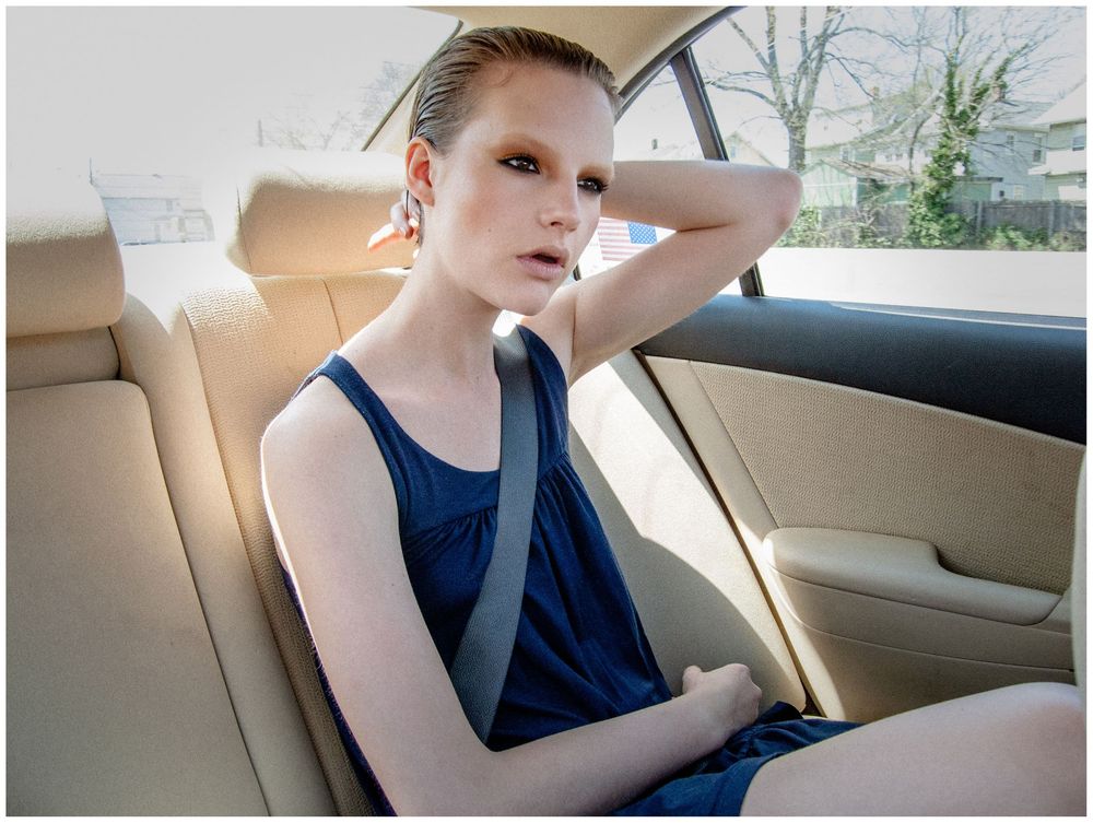 Young woman in navy blue tank top sitting in beige leather car seat looking at camera.
