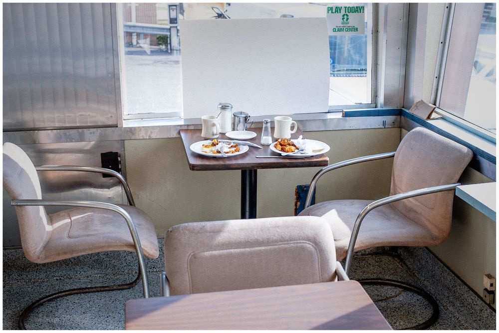 Cozy diner booth with two upholstered chairs at a small table set with plates and glasses near a window.