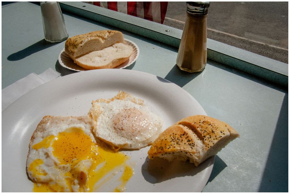 Breakfast plate with fried eggs and toast served at a diner with bread basket and pepper shaker visible.
