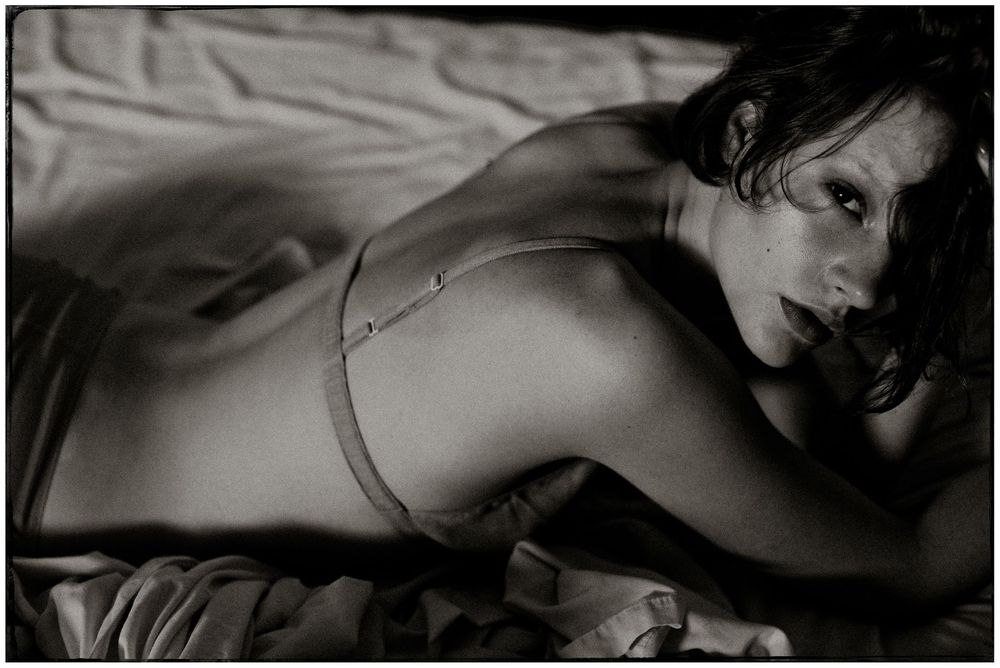 Black and white photograph of a woman in lingerie reclining on a bed.