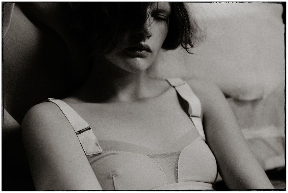 Vintage black and white photo of a young woman wearing a classic white brassiere in soft light.