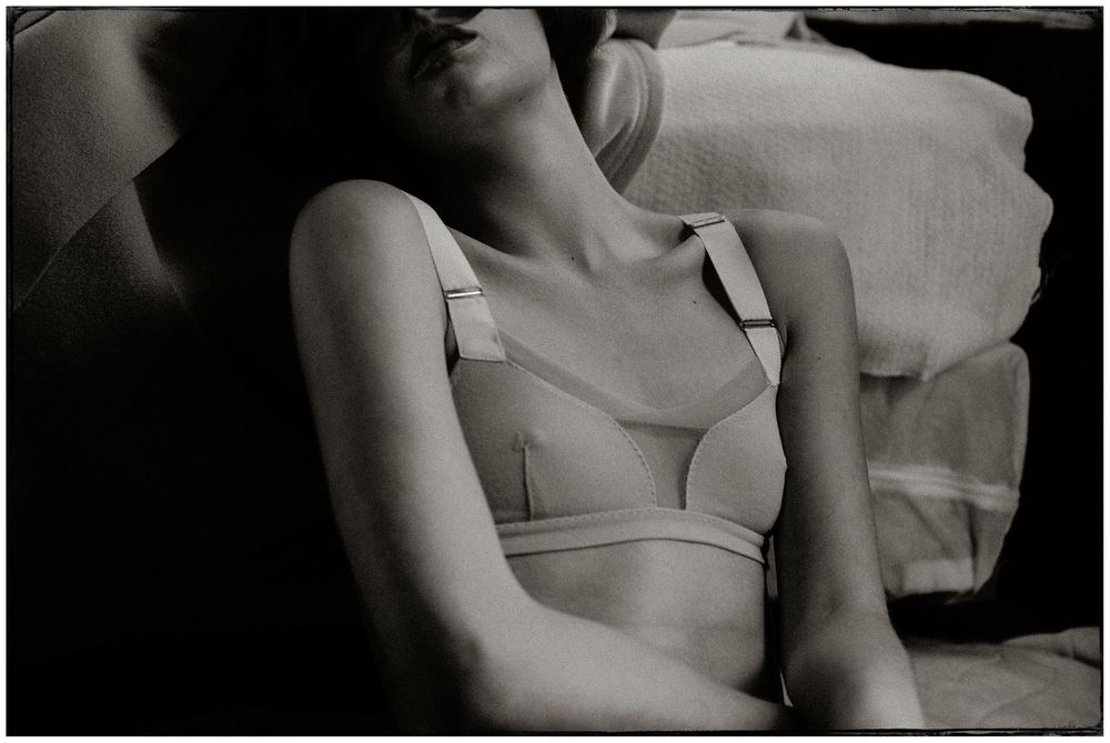 Black and white photo of a woman in a bra reclining on a sofa with head tilted back.