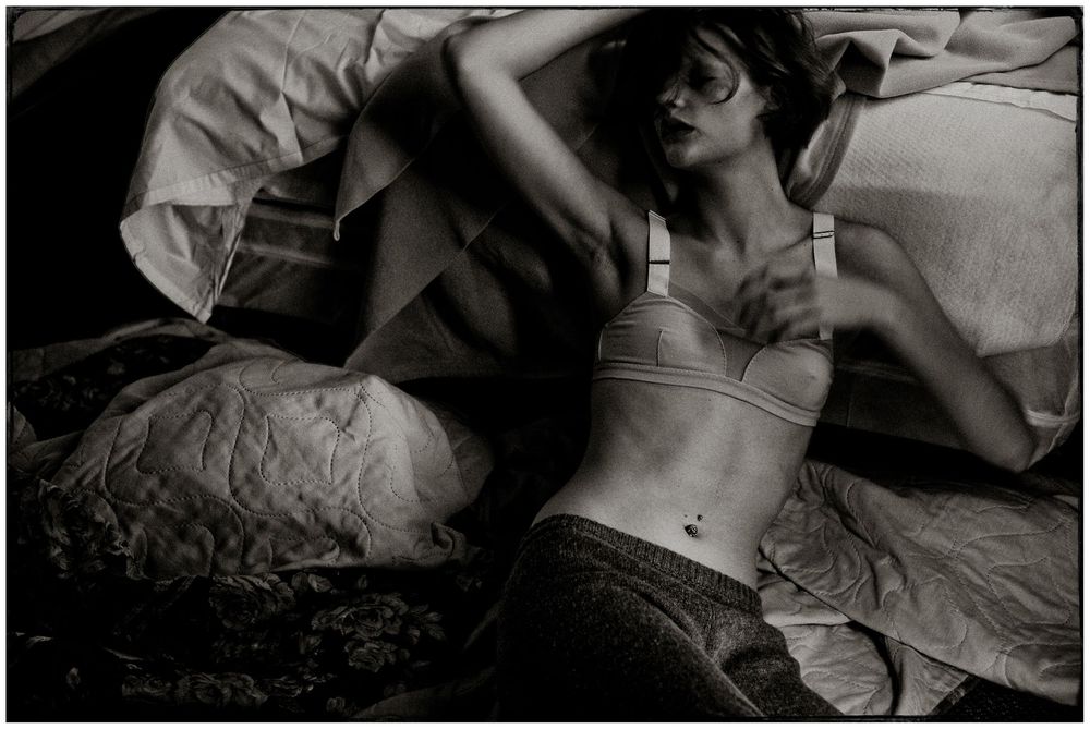 Black and white photograph of a person in contemplative pose on a bed.
