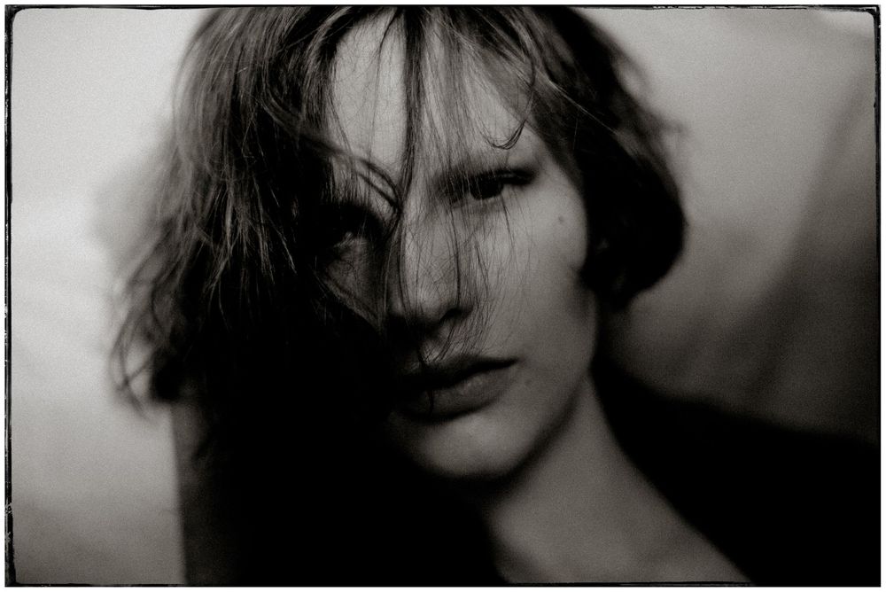 Black and white portrait of a person with tousled dark hair and intense gaze, shot in moody atmospheric lighting.
