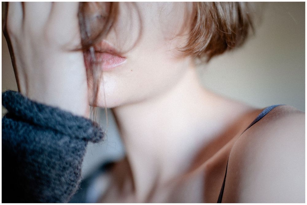 Close-up portrait of a young woman with short hair holding a gray knit fabric near her face.