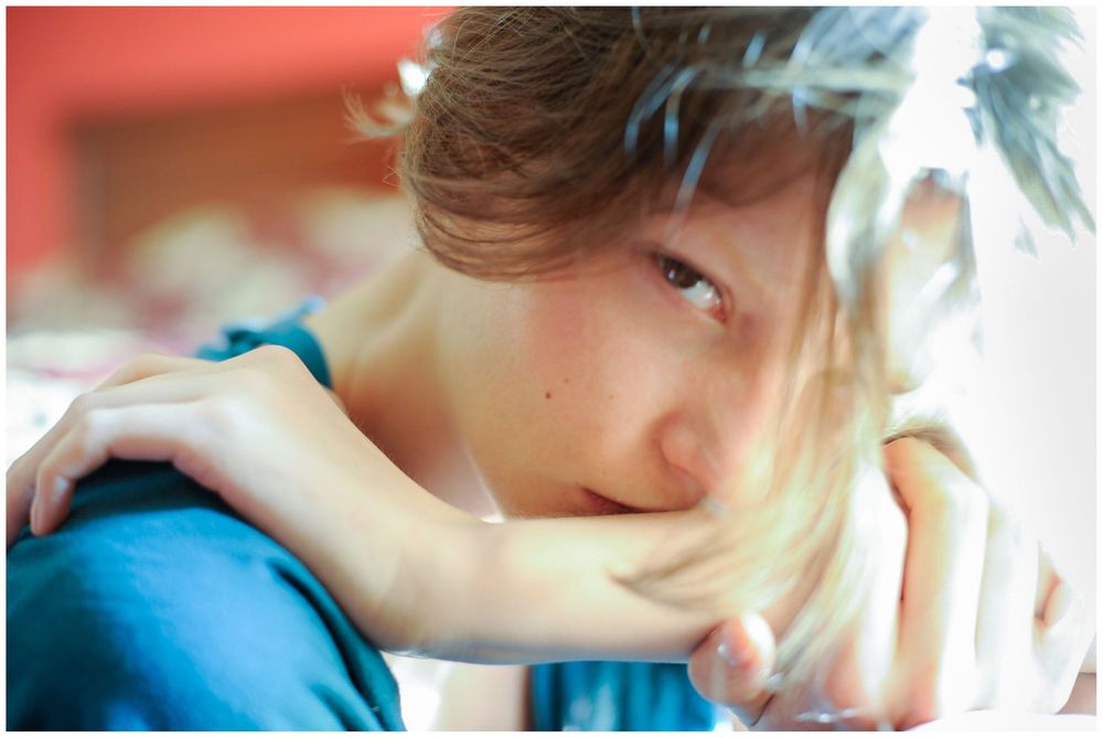Young person in a teal shirt resting chin on arm with a thoughtful, contemplative expression.