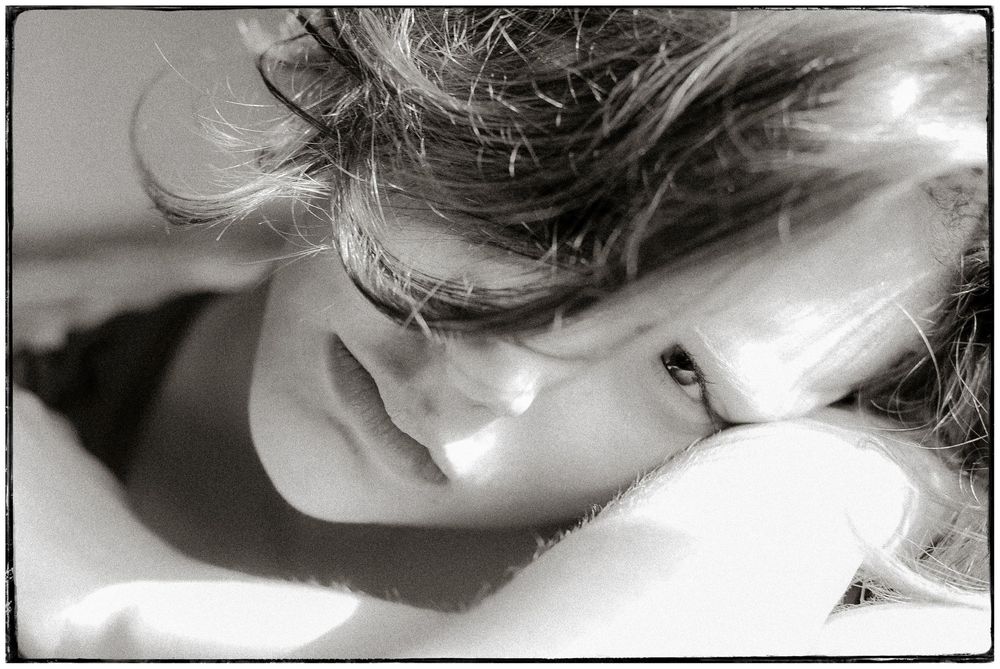 Black and white photo of a person resting their head on their arm in soft sunlight.