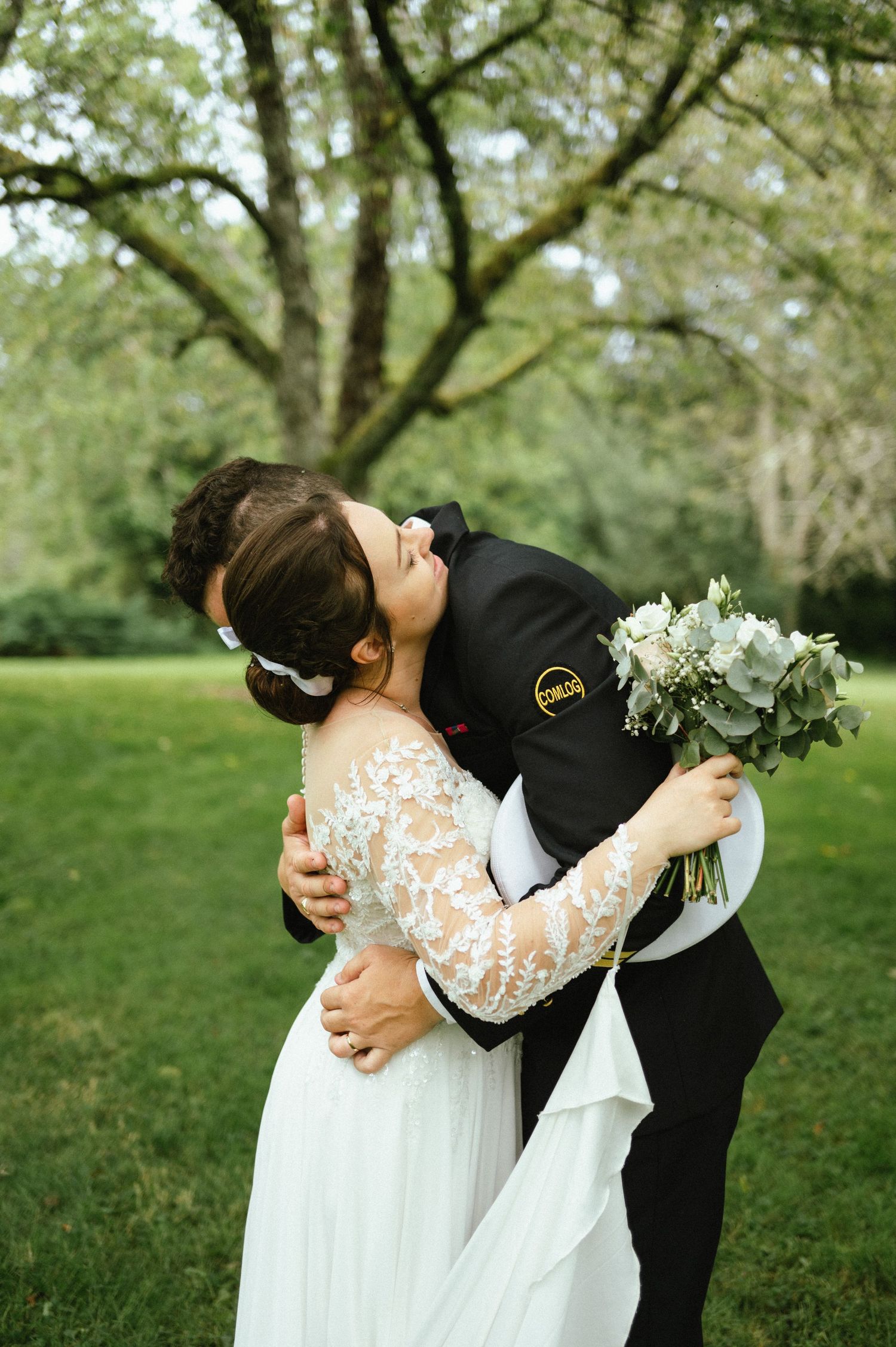 A romantic wedding couple shares an intimate dip kiss in a lush green garden setting.