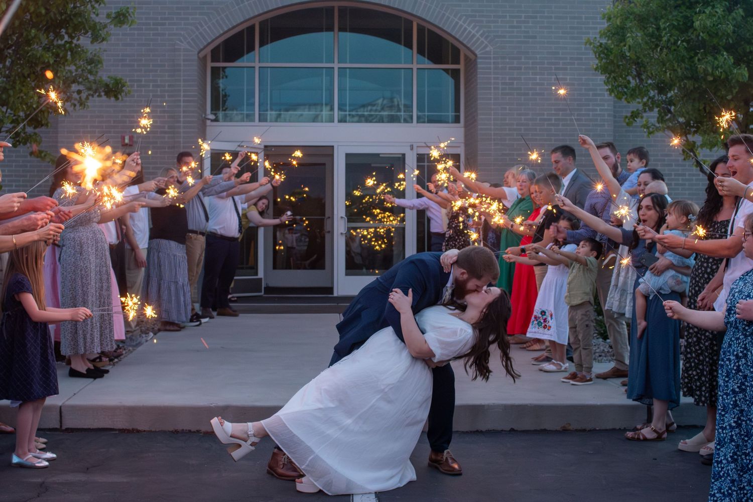 Wedding guests hold sparklers creating a magical light tunnel for the newlyweds during an evening outdoor celebration.
