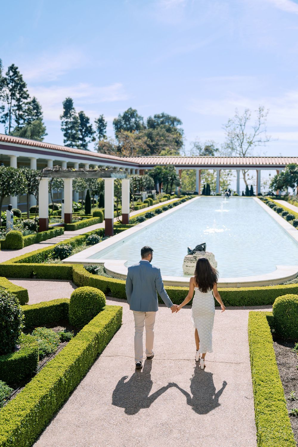 A couple walks along a manicured garden path beside a reflecting pool at the Getty Villa in Los Angeles.