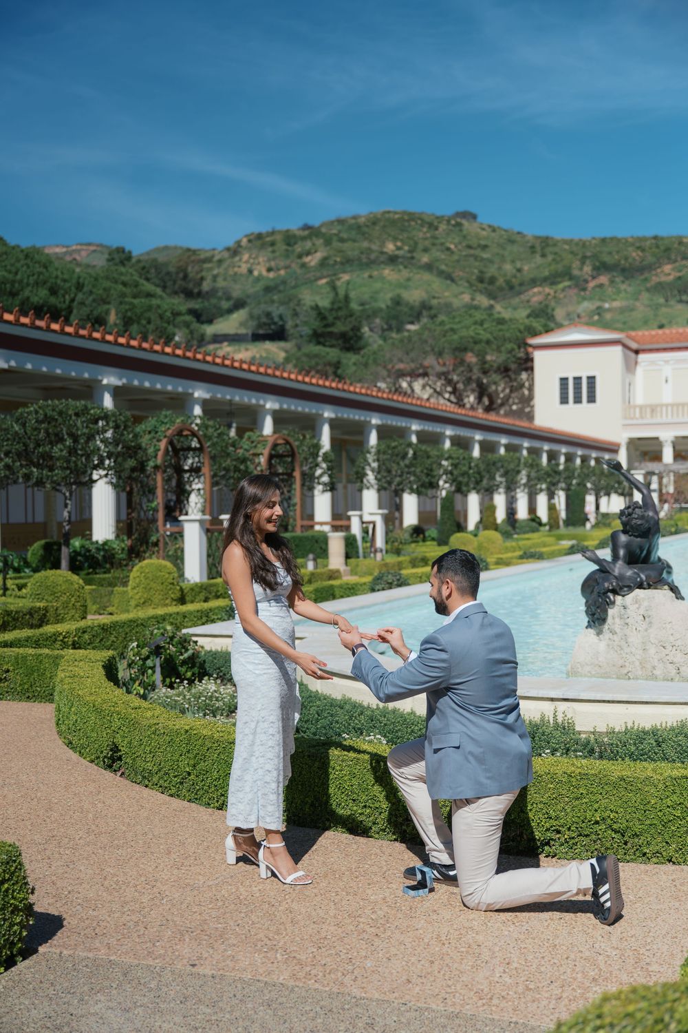 A romantic proposal moment in a beautiful garden courtyard with manicured hedges and a fountain at the Getty Villa.