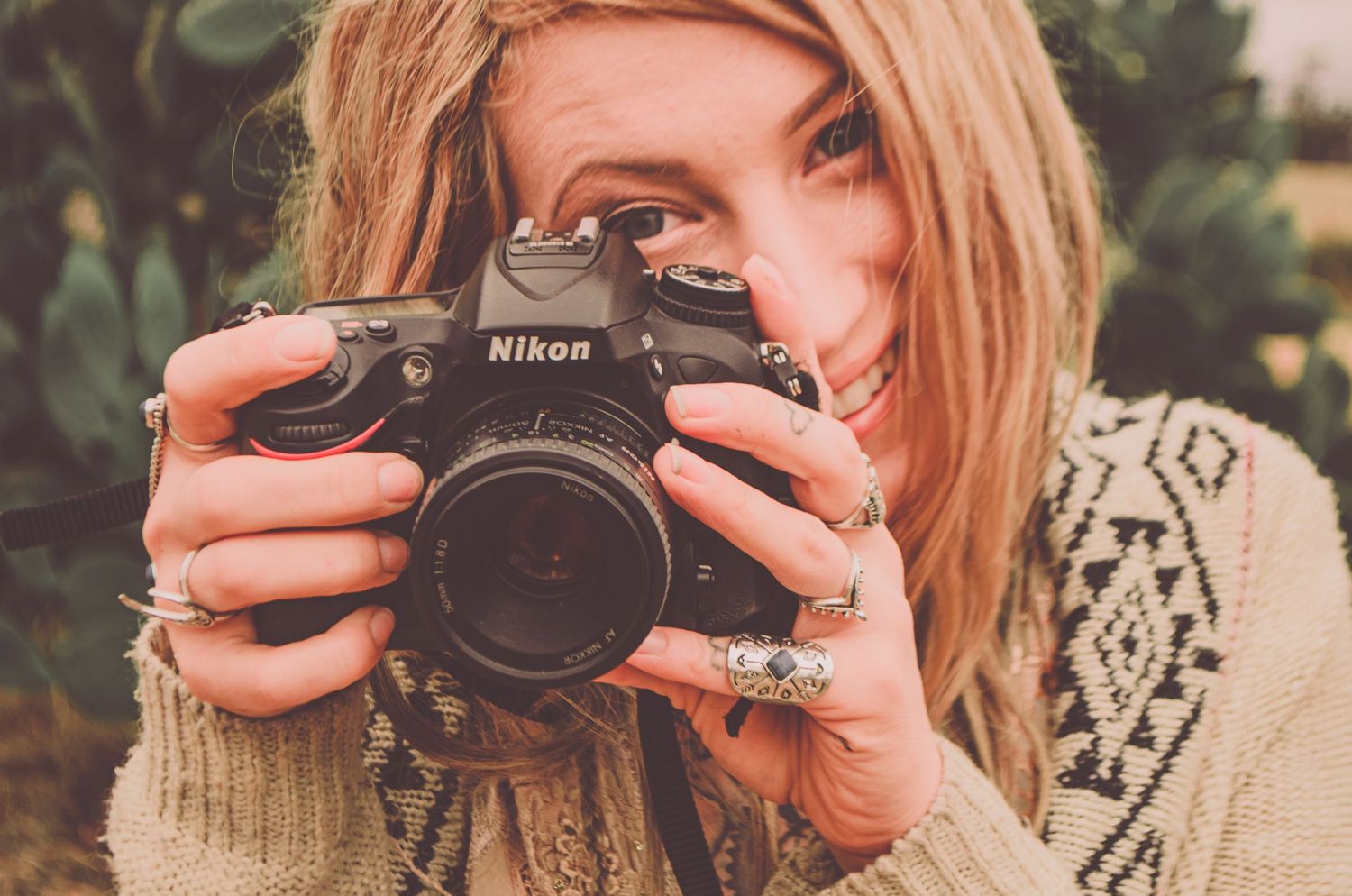 A photographer with a Nikon DSLR camera takes a photo against a backdrop of vibrant pink flowers.