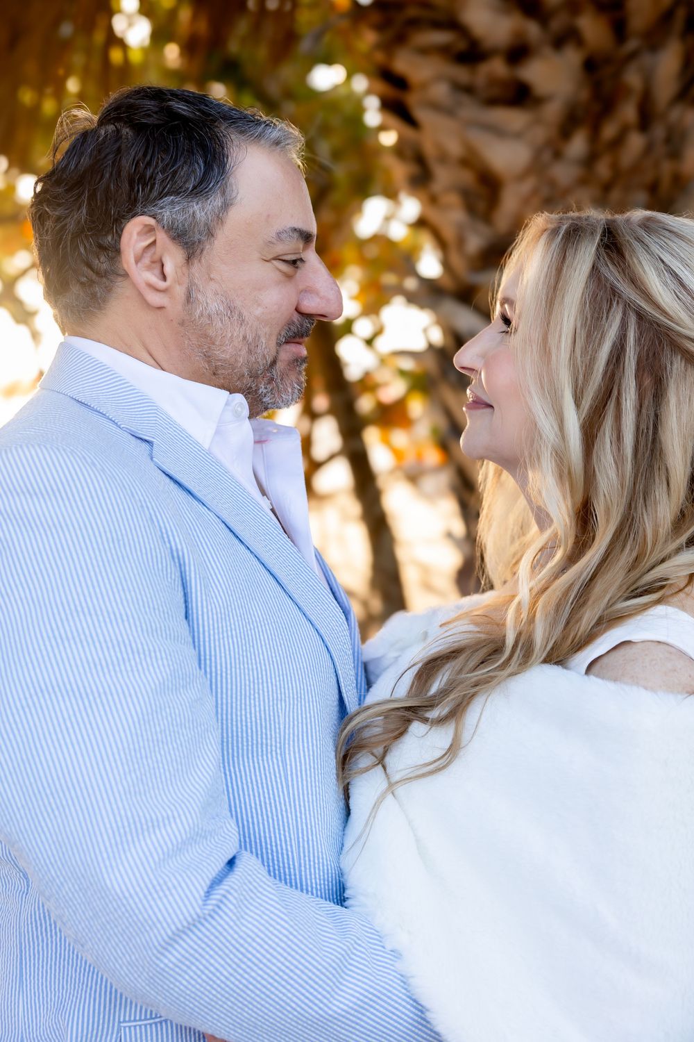 Romantic wedding couple gazing into each others eyes beneath a sunlit palm tree at golden hour.