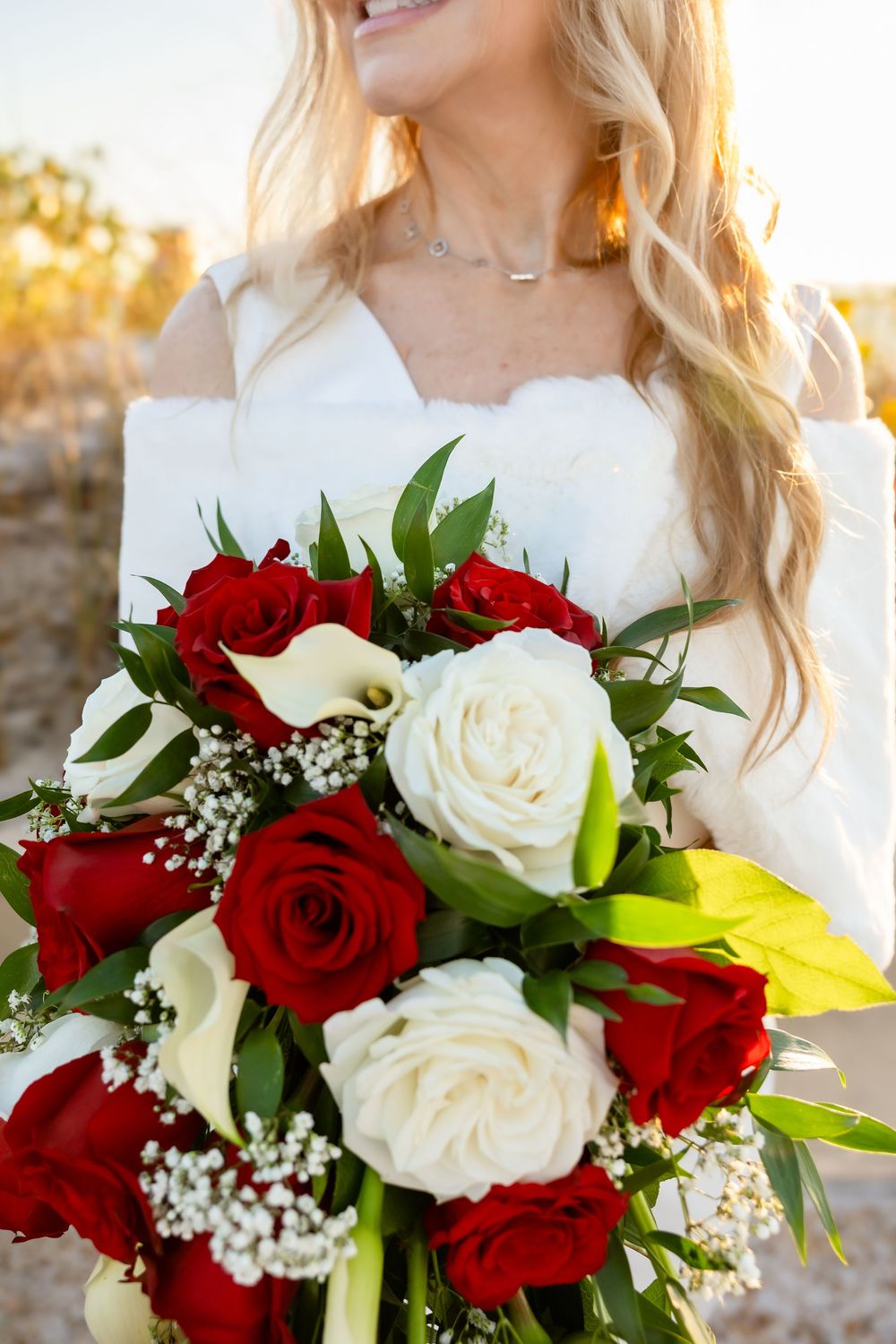 Close-up of a bridal bouquet featuring red roses, white roses, calla lilies, and baby's breath.