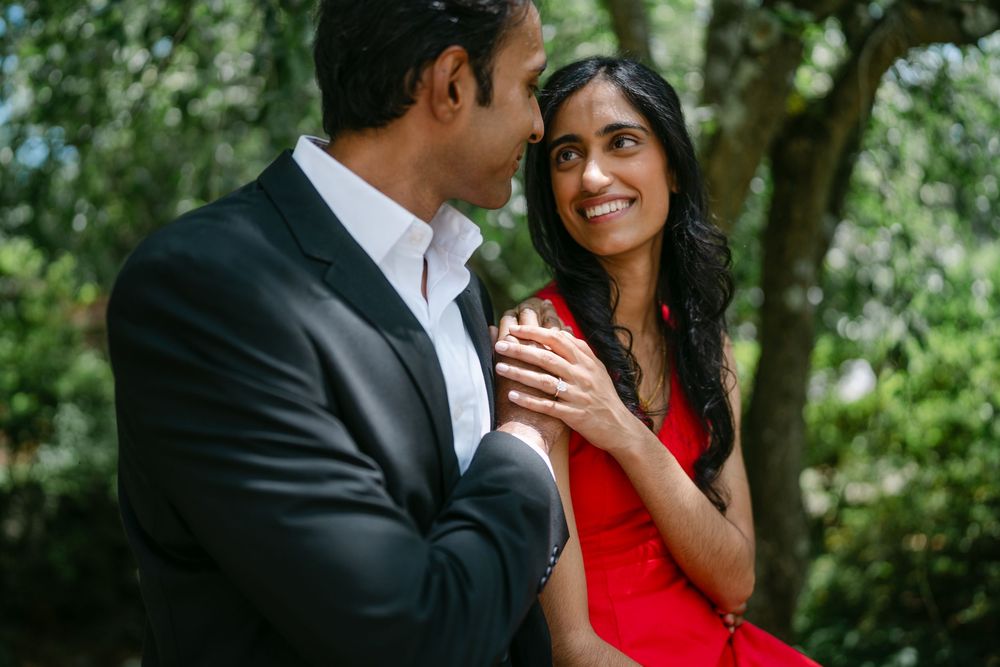 A couple in formal attire shares romantic moments in a lush outdoor garden setting during their engagement photoshoot.