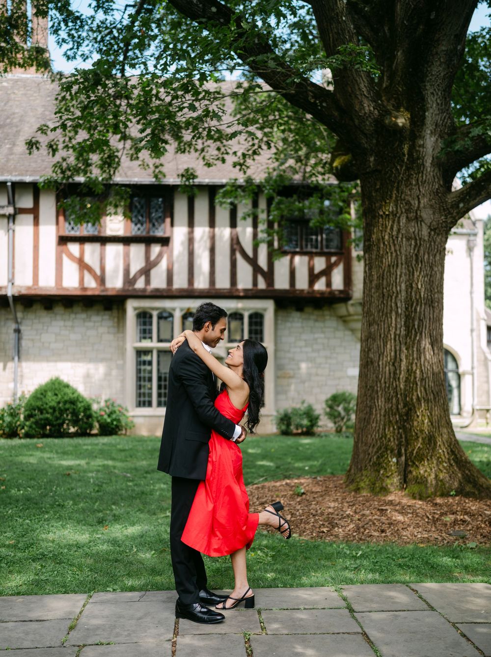 A couple in formal attire dances gracefully on a stone pathway near a historic building with trees.