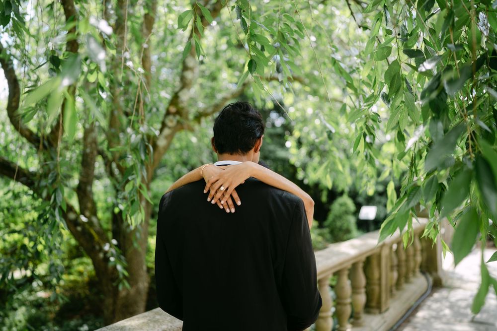 Couple walking hand in hand down a romantic tree-lined pathway surrounded by lush green foliage.