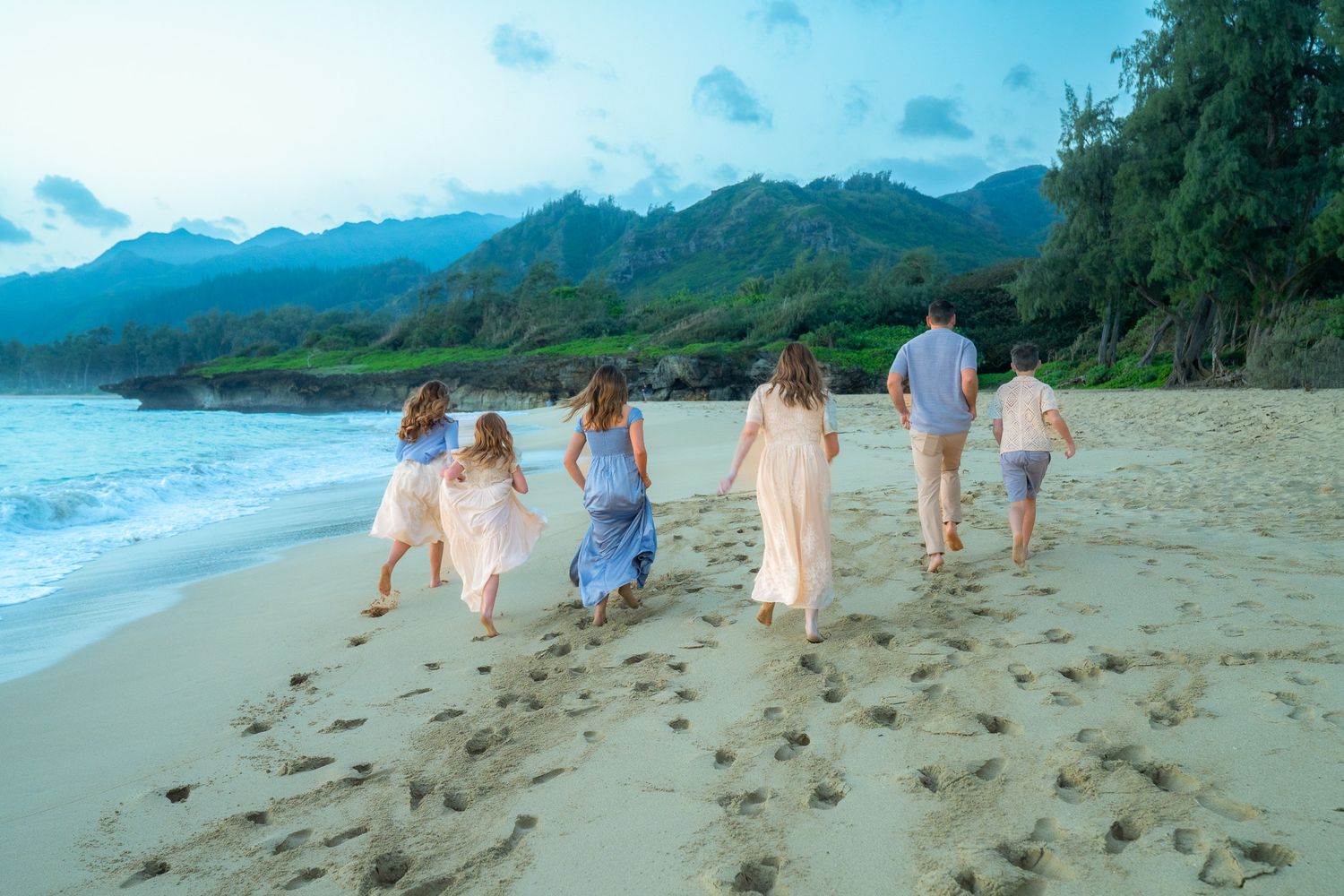 People walking together on a scenic tropical beach with mountains in the background at sunset.