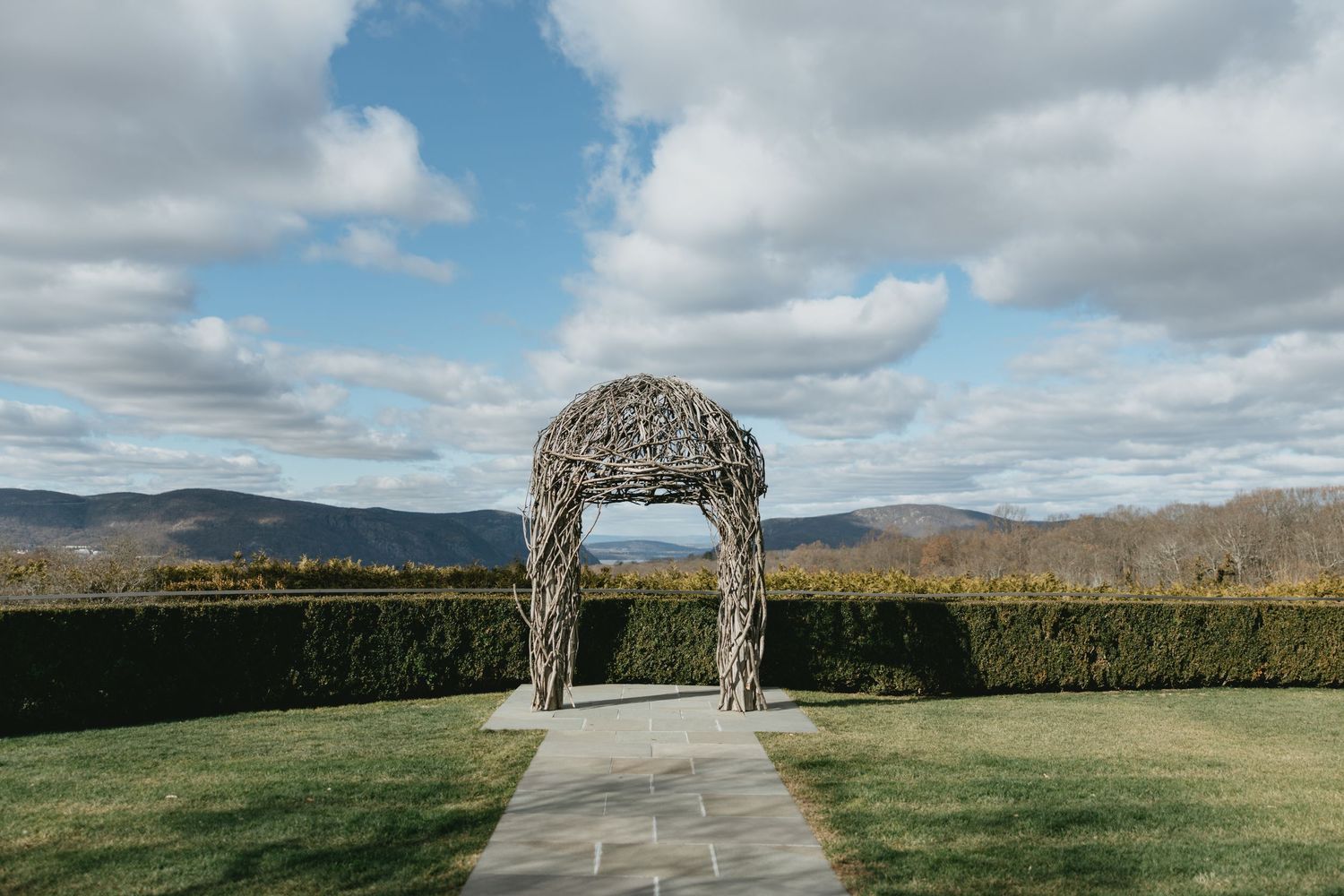 Wedding ceremony setup with white chairs on a lush green lawn facing a historic stone church under cloudy skies.