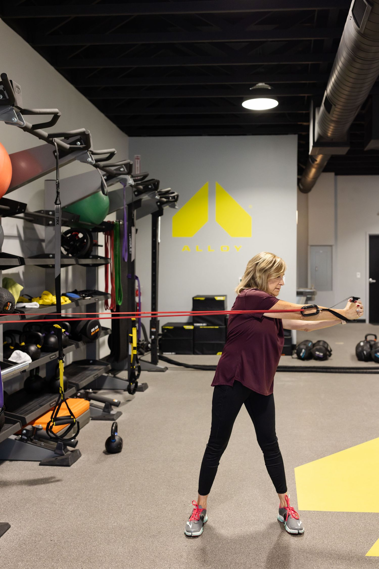 Someone exercises with resistance bands in a modern fitness facility with yellow branding and workout equipment.