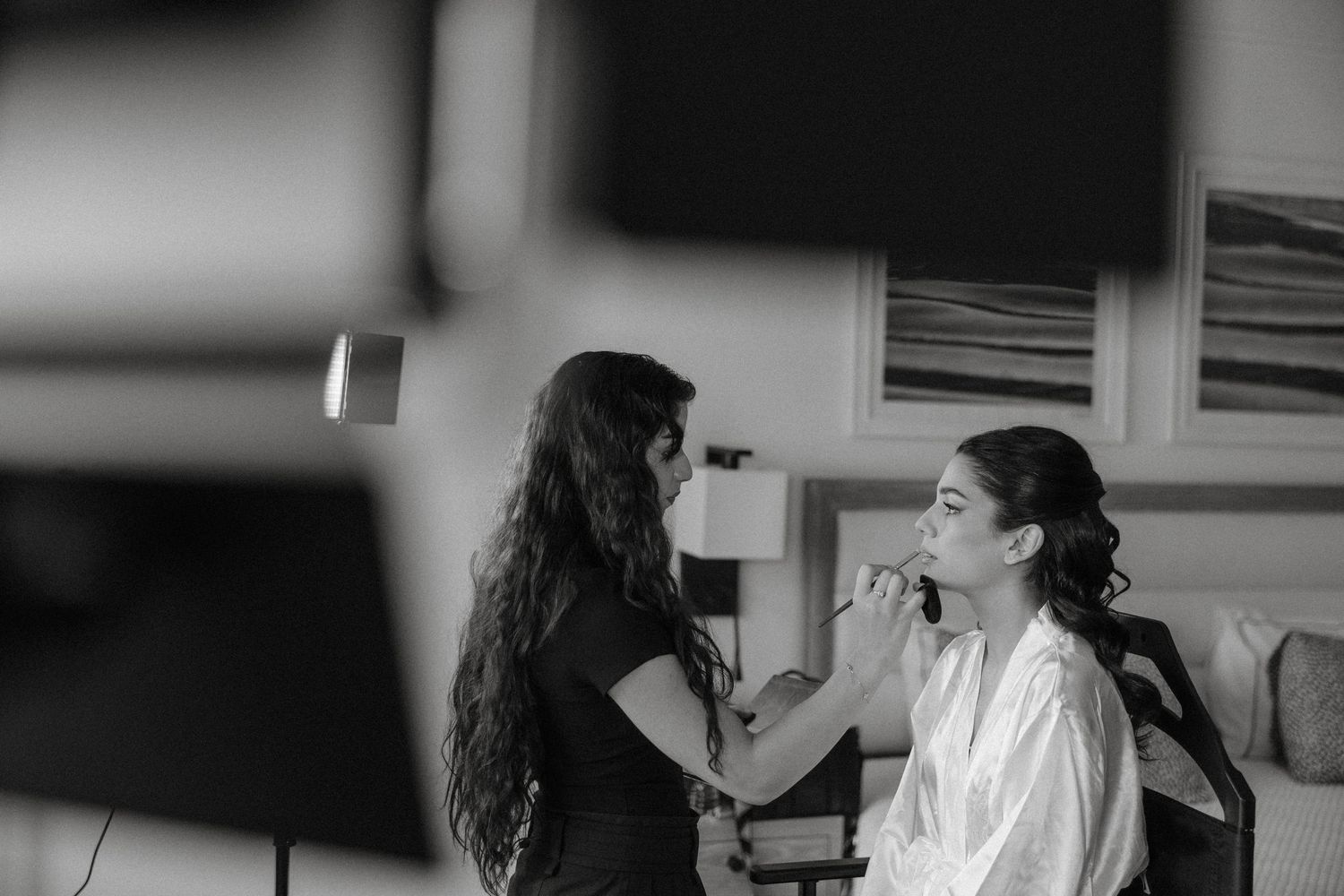 A makeup artist applies cosmetics to a bride in Cyprus in a black and white photograph.