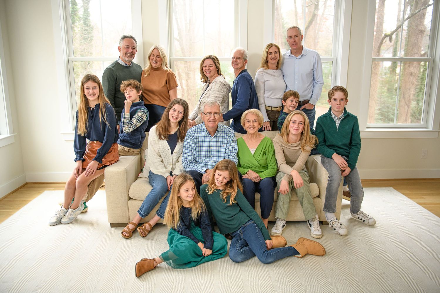 Large multi-generational family group poses together for a portrait in a bright sunlit room.