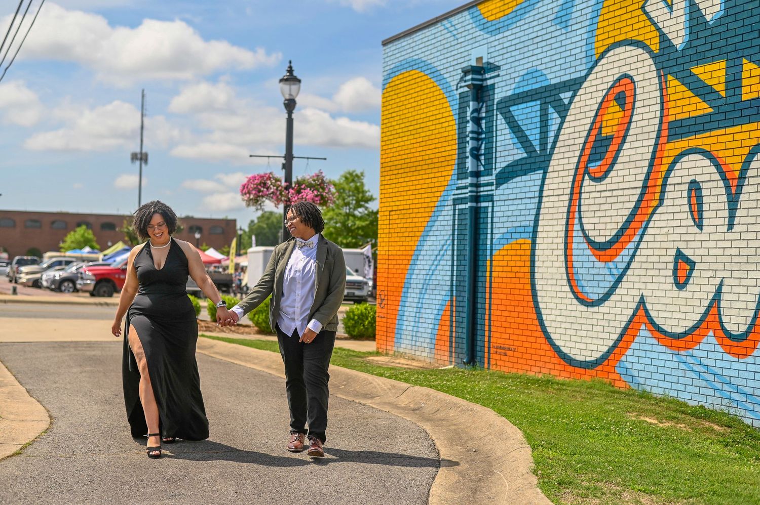 Two women in formal attire walking past a vibrant colorful graffiti mural outdoors.