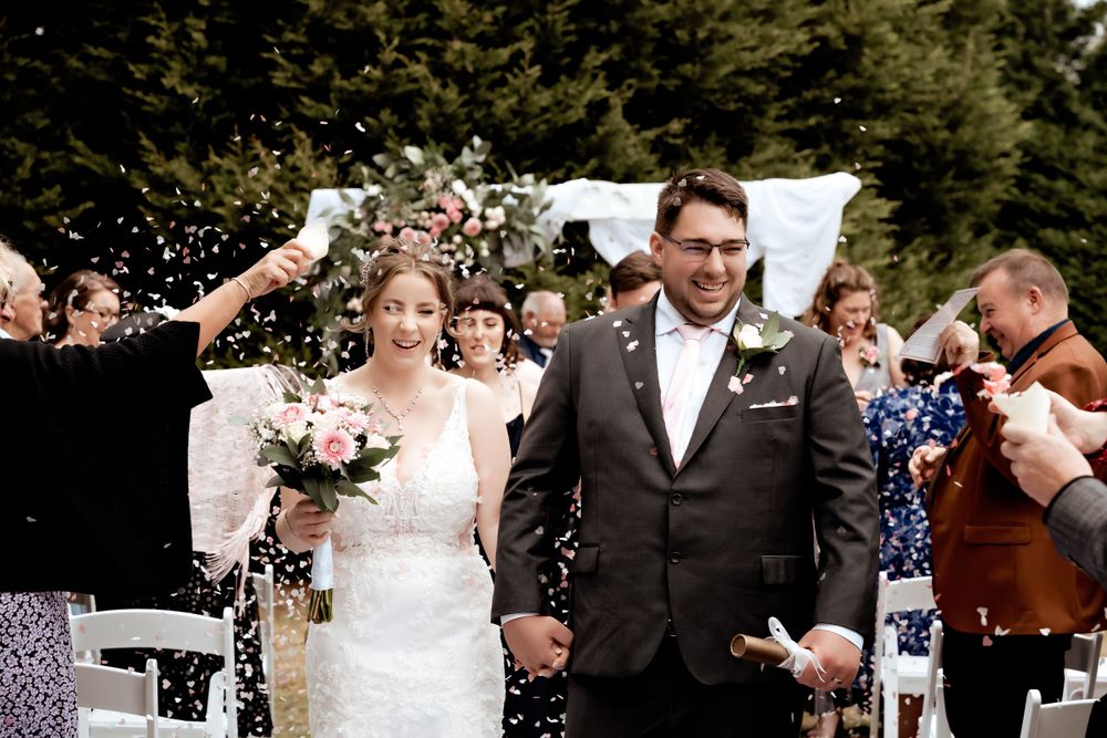 Wedding couple walks down aisle while guests throw confetti in celebration.