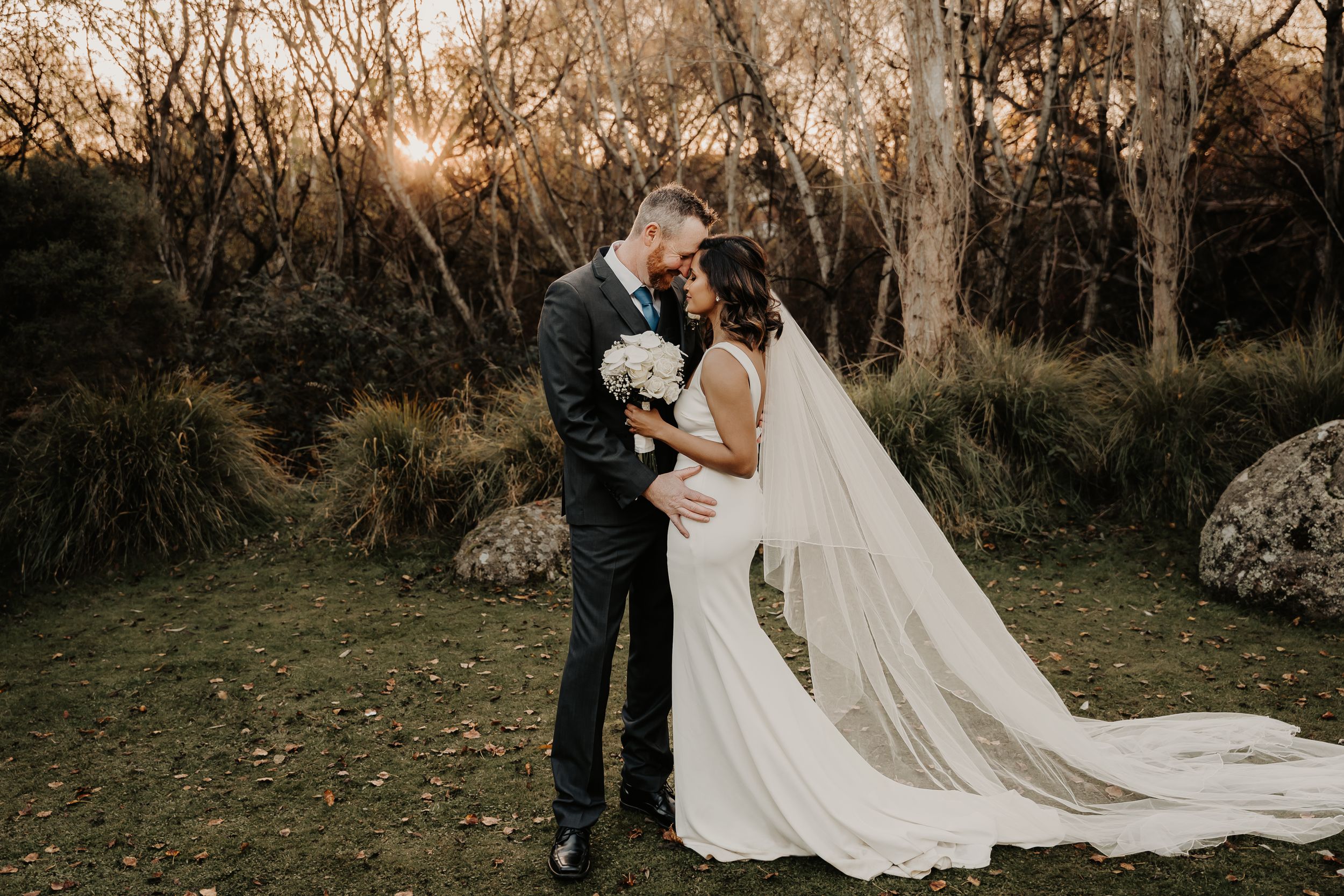 Wedding couple shares intimate moment at sunset in wooded natural setting.