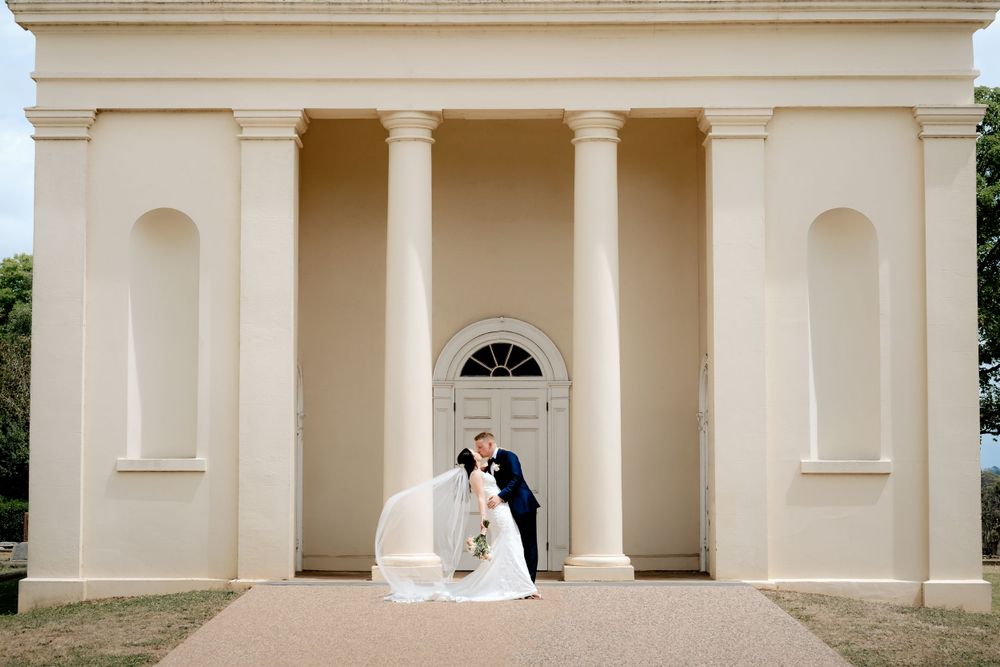 Elegant wedding couple poses in front of a classical columned building entrance with cream colored walls.