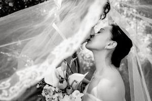 Romantic black and white portrait of wedding couple sharing intimate moment under veil.