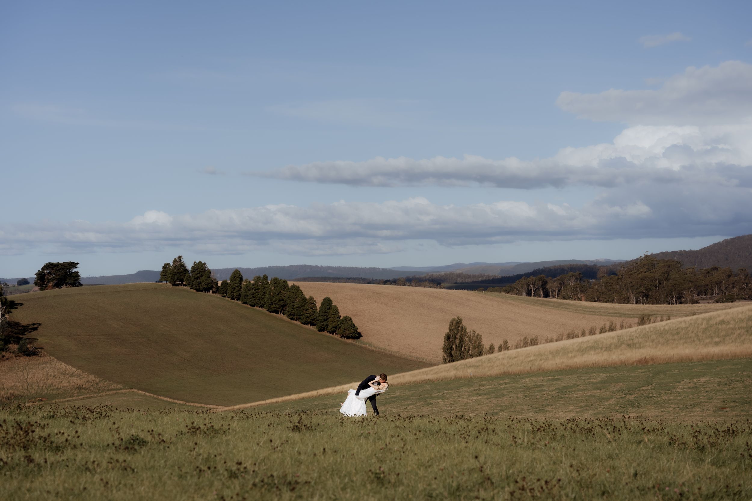 Rolling hills and grasslands stretch across a vast landscape under partly cloudy skies.