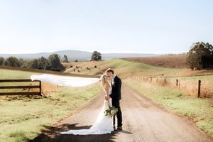A couple shares a romantic moment on a winding dirt road through rolling countryside hills on a sunny day.