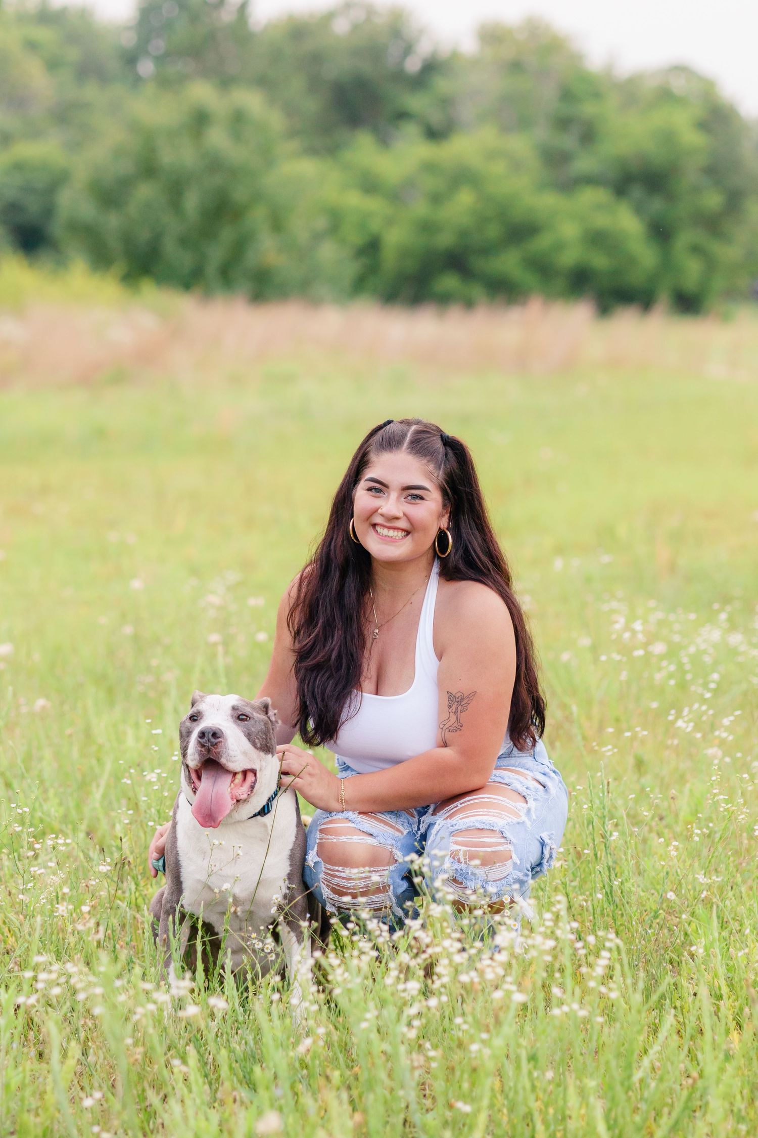 A woman sits with her smiling pitbull dog in a wildflower meadow on a sunny day.