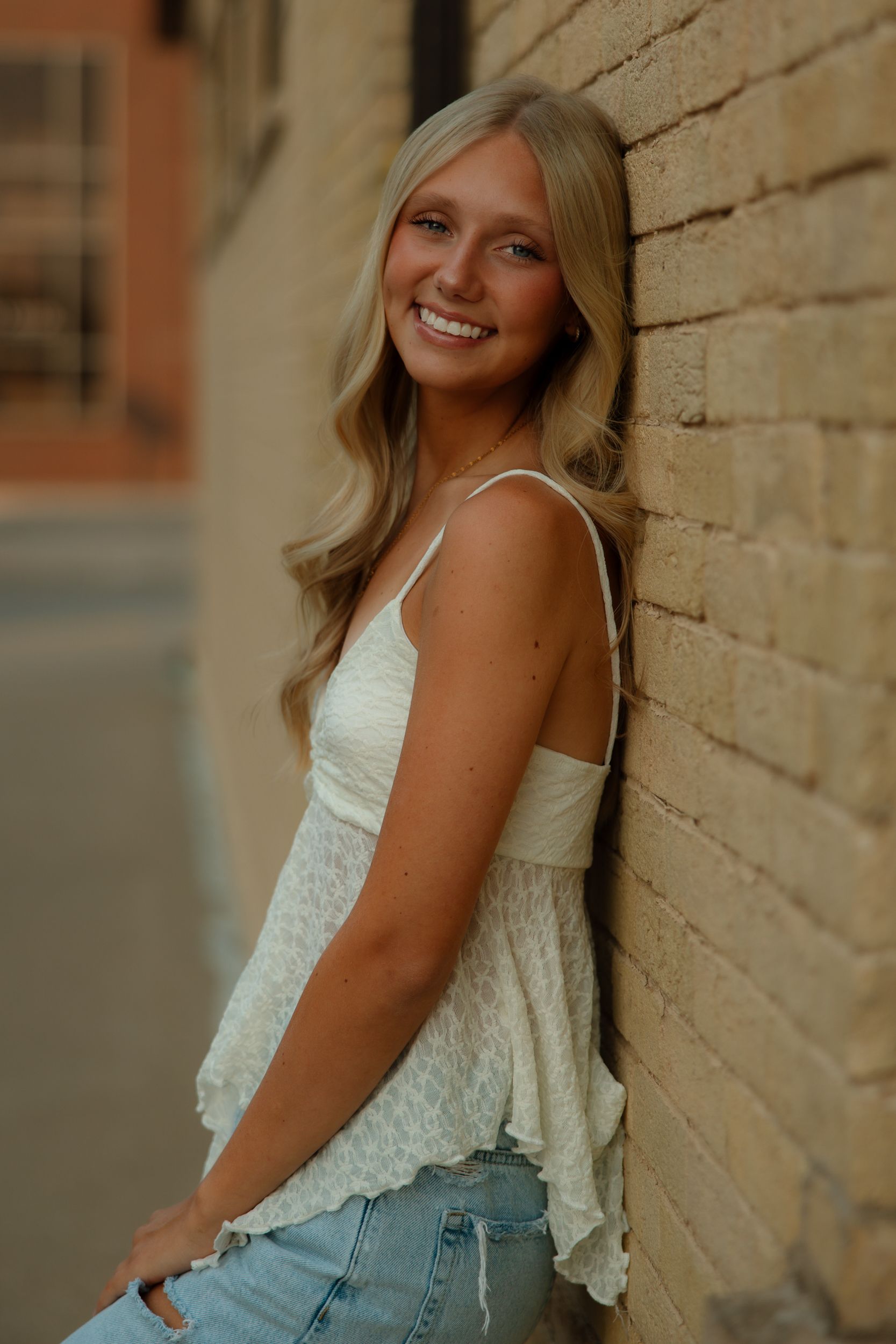 A person in a white lace top and denim poses against a brick wall in a casual summer portrait series.