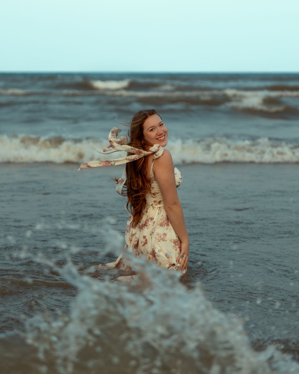 A person in a floral dress dances and twirls gracefully along the beach shoreline at sunset.