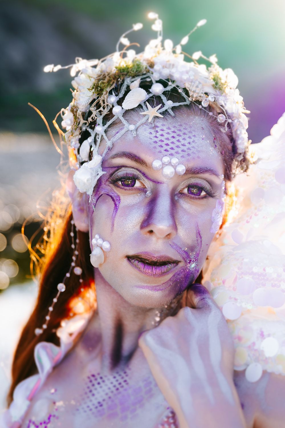 Artistic fantasy makeup with white flowers, purple accents, and pearl details creates an ethereal beauty look.