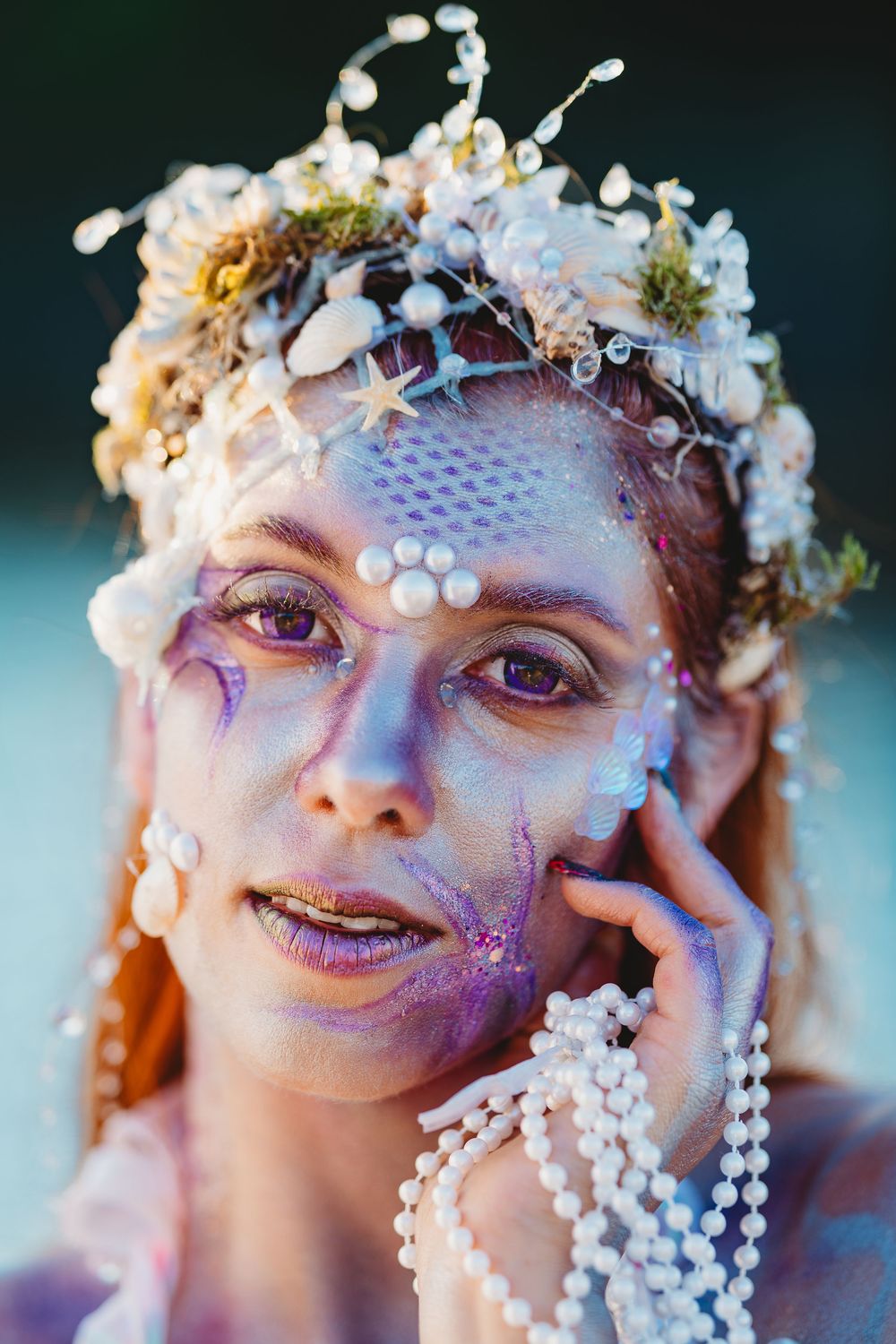 Ethereal fantasy makeup look with white flowers, pearls and glitter in shades of purple and blue creating a magical effect.