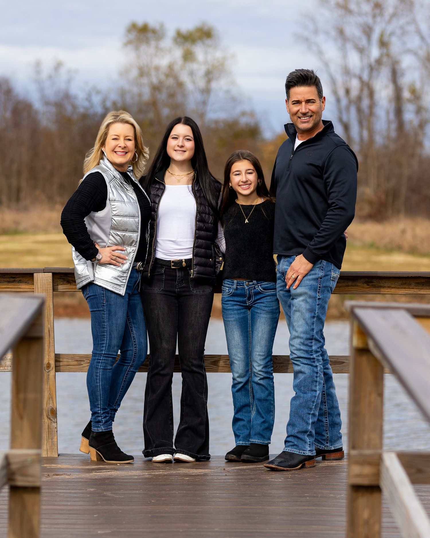 A family of four poses together on a wooden deck bridge during an autumn day.