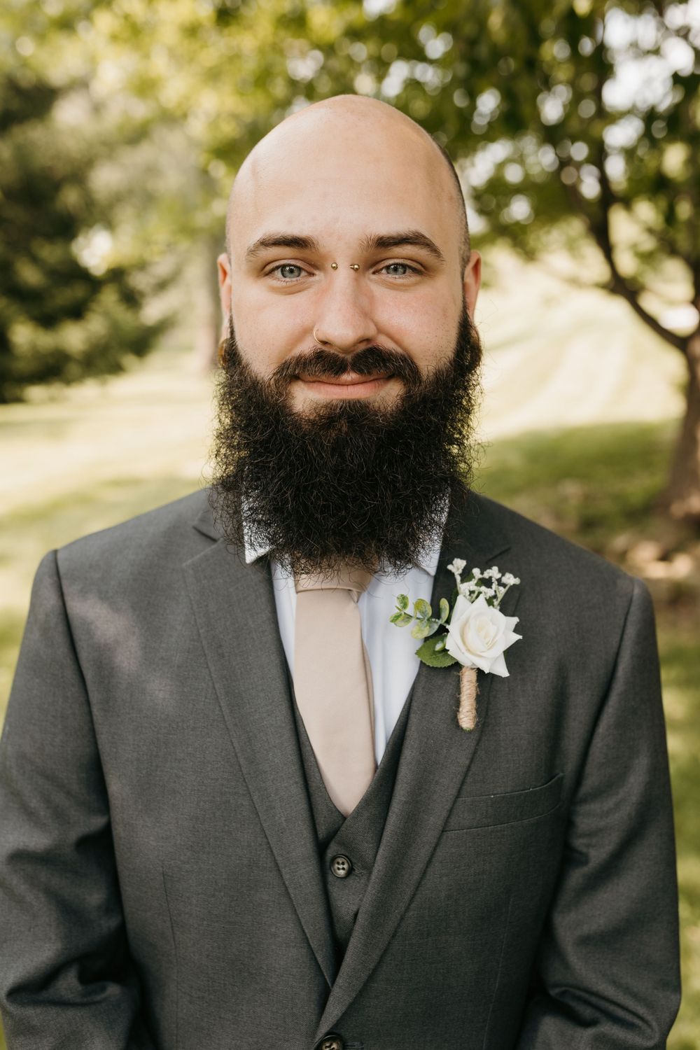 Close-up portrait of bald groom with dark beard wearing gray suit and white rose boutonniere.