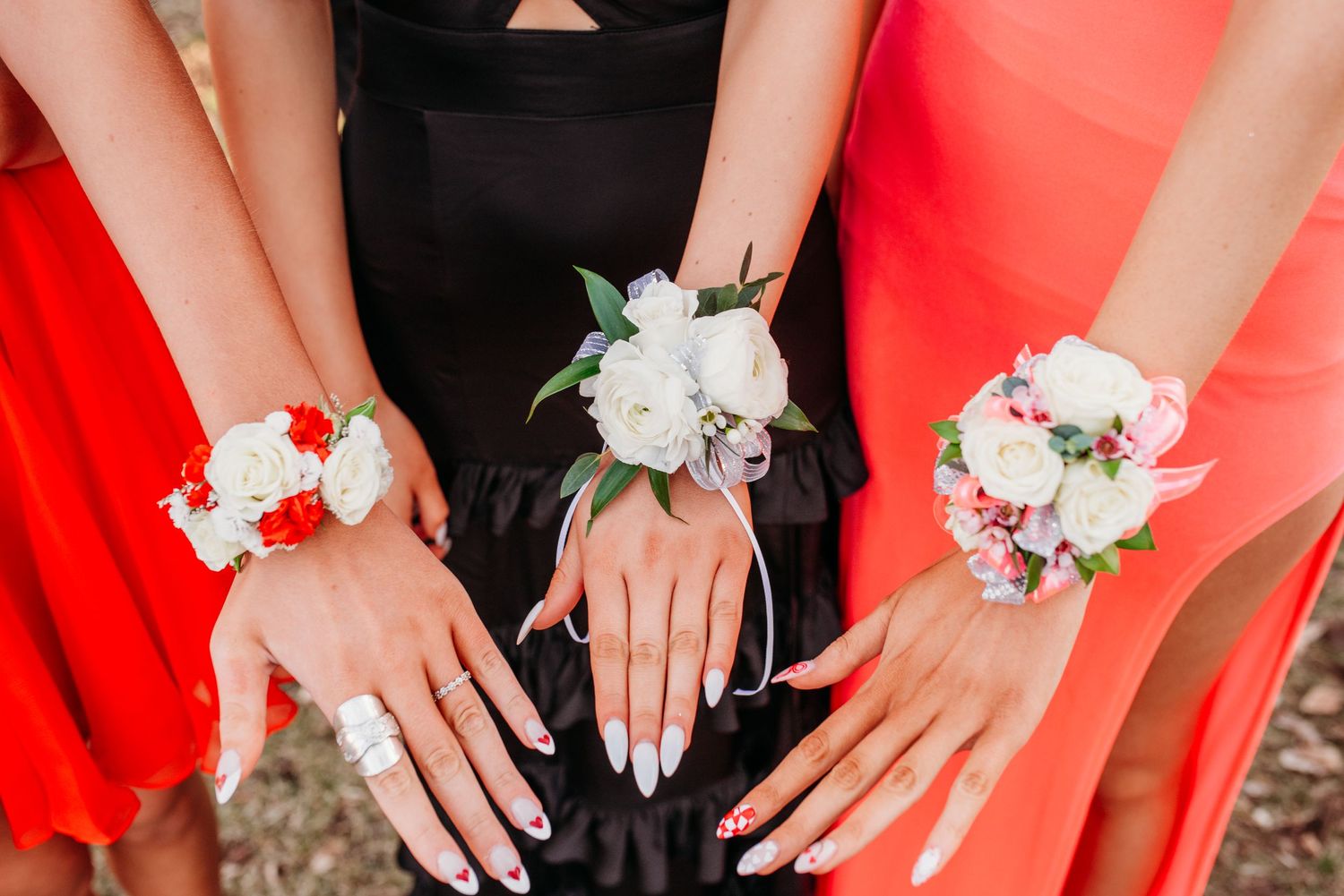Close-up of three hands wearing floral corsages in red and white against formal dresses.