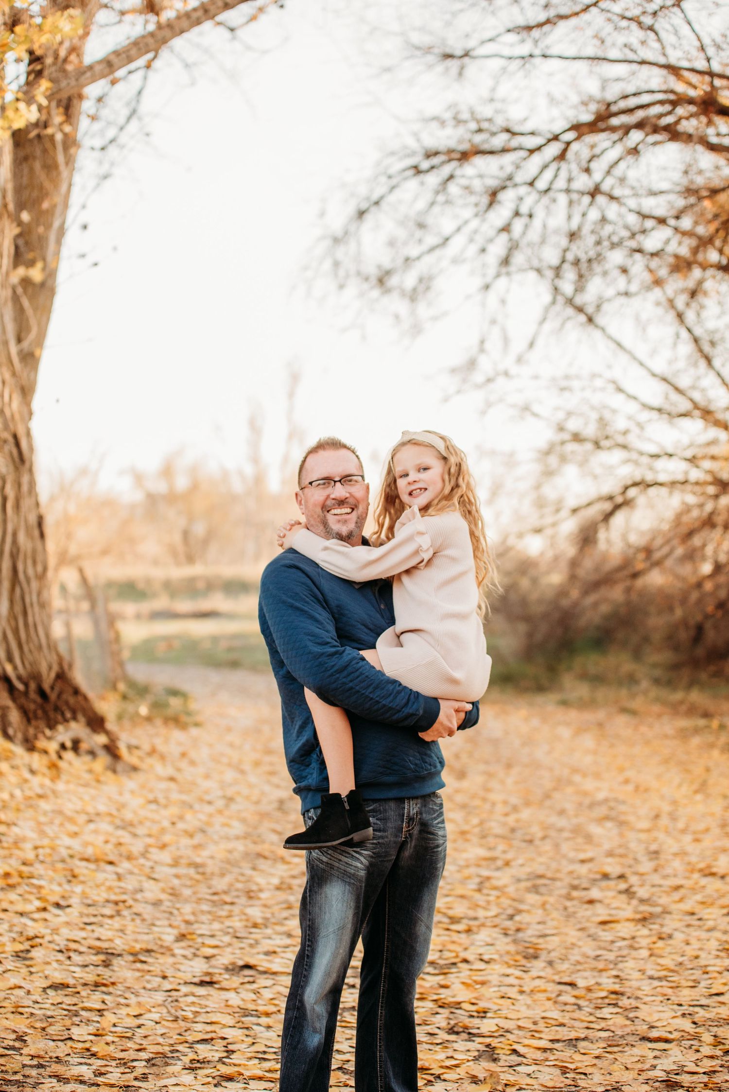 A warm autumn portrait taken outdoors with fallen leaves and bare trees in the background.