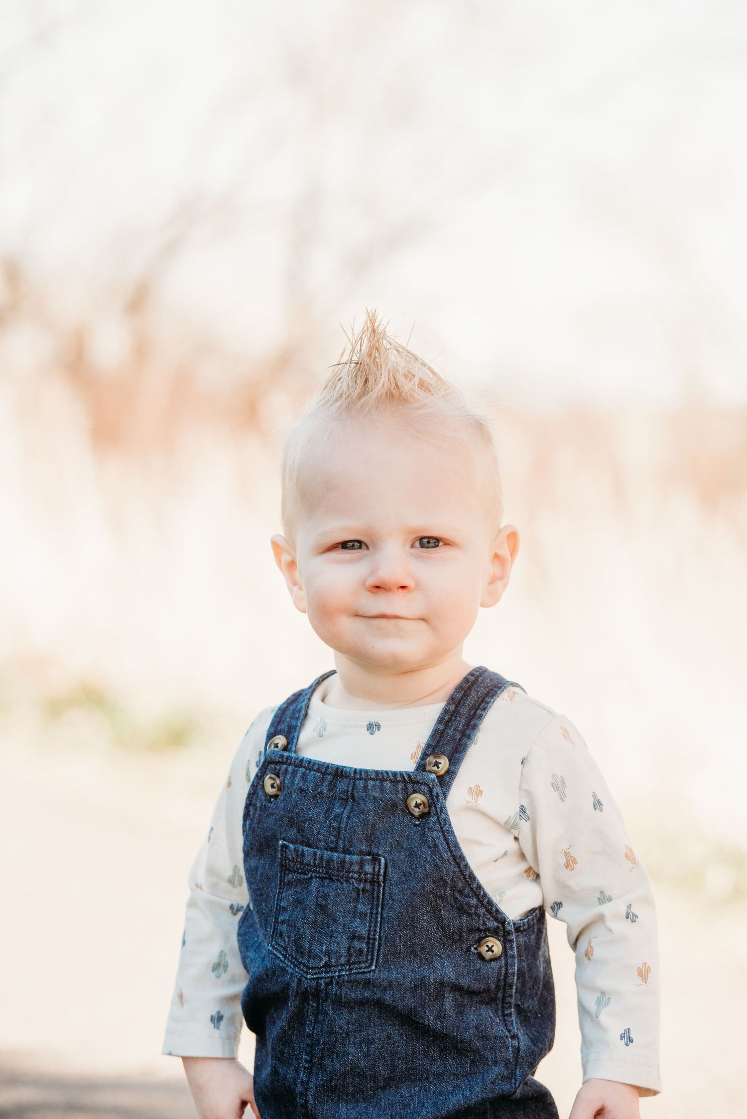 Toddler in denim overalls smiling at camera with soft focus background.