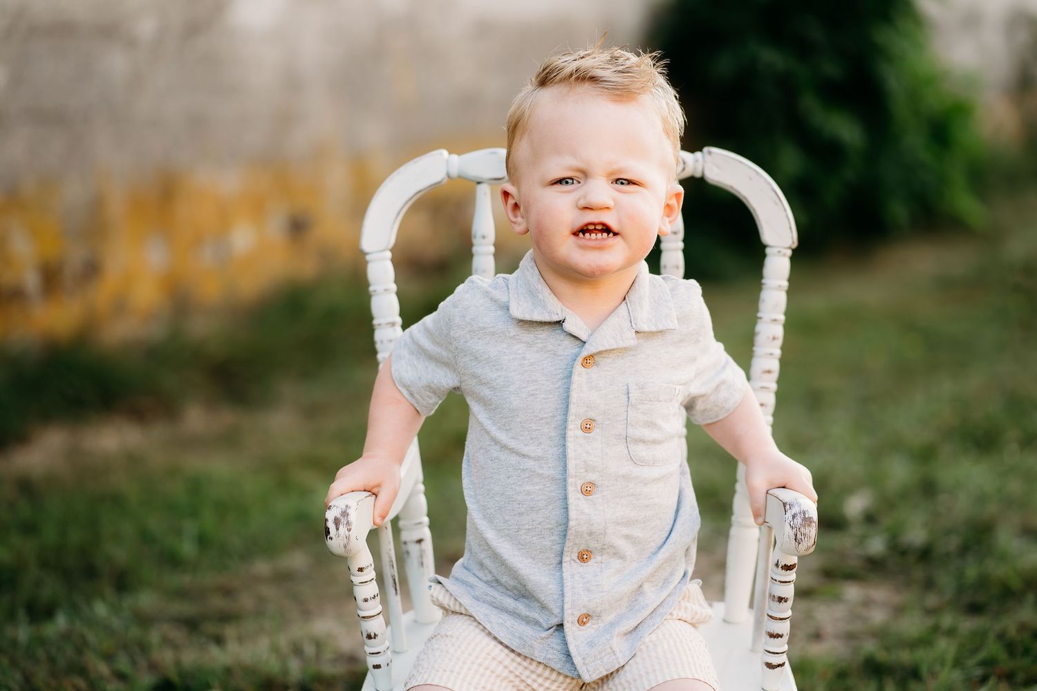 Toddler boy sits in rustic rocking chair sat in the grass for summer family photos at Nisqually Wildlife Refuge.